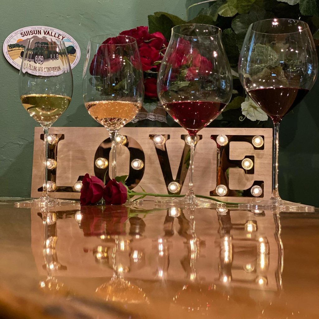 four wine glasses with a lighted LOVE sign behind them celebrating Valentine's Day at Suisun Valley Filling Station in Fairfield, CA